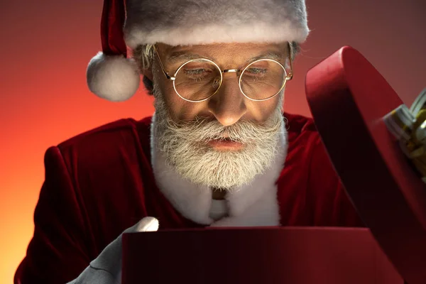 Пожилой Санта Клаус заглянул в открытую коробку с подарками — стоковое фото