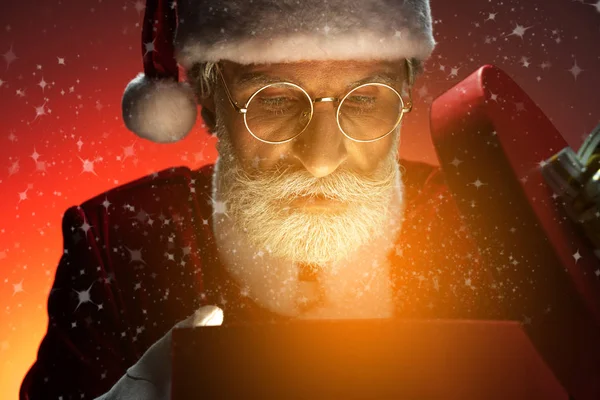 Santa Claus looking at opened gift box with magic light — Stock Photo, Image