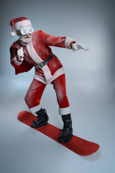 Senior Santa Claus sosteniendo saco, de pie sobre tabla de snowboard — Foto de Stock
