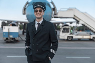 Havaalanında yürüyen üniformalı yakışıklı gülümseyen pilot