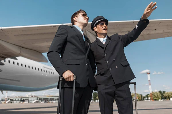 Reifer Pilot zeigt seinem Kollegen am Flughafen etwas — Stockfoto