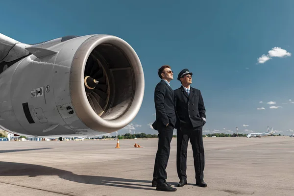 Knappe volwassen collega's staande in de buurt van de motor van het vliegtuig — Stockfoto