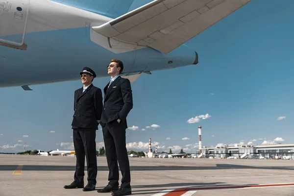 Volwassen mannen in uniform staande onder vleugel van het vliegtuig — Stockfoto