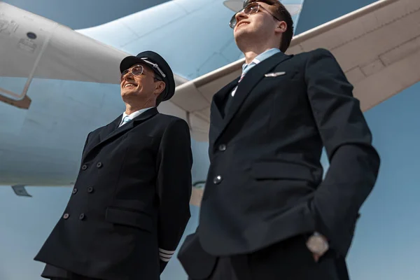 Vrolijke mannen in uniform staande onder vleugel van het vliegtuig — Stockfoto