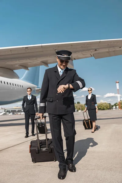 Knappe blanke piloot kijken naar het horloge in de luchthaven — Stockfoto