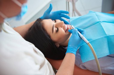 Koruyucu maskeli erkek diş hekimi güzel bayan için diş temizliği yapıyor