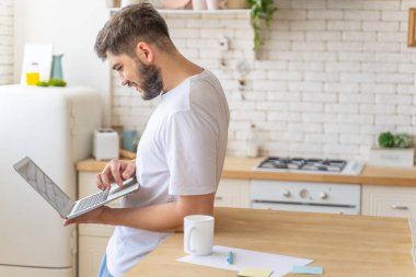 Mutfakta dizüstü bilgisayar tutan gülümseyen genç adam