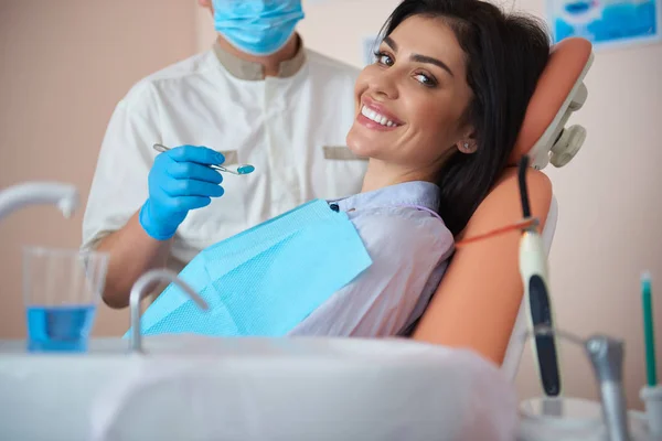 Encantadora joven dama está visitando dentista y sonriendo —  Fotos de Stock