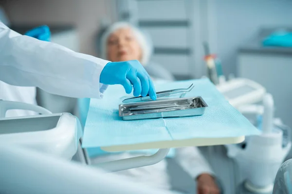 Dentista em luvas estéreis tomando instrumentos cirúrgicos dentários — Fotografia de Stock
