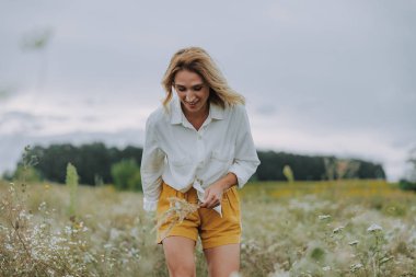 Güzel kadın açık havada yabani çiçekler topluyor