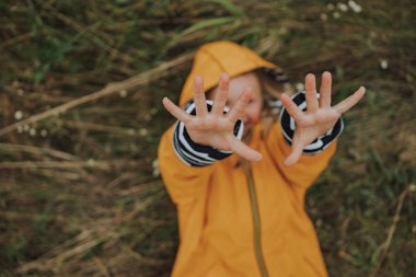 Yağmurluklu gülümseyen küçük çocuk dışarıda yatıyor.