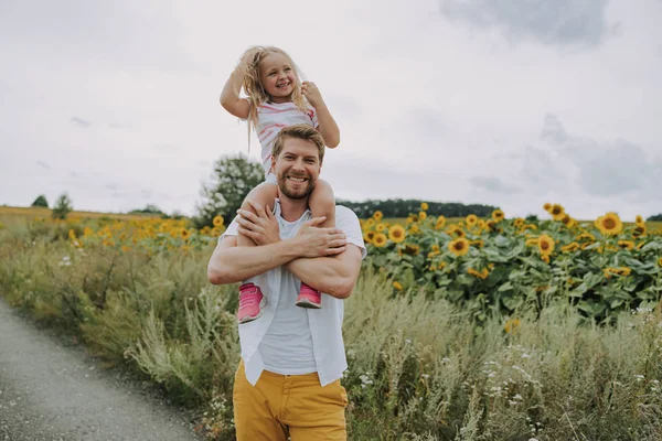 Pequena filha alegre se divertindo com seu pai sorridente perto do campo — Fotografia de Stock
