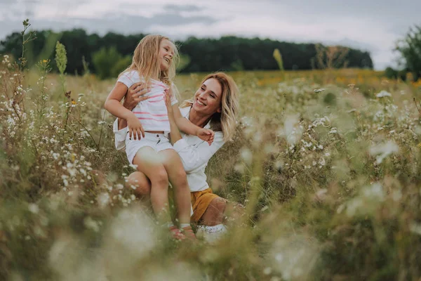 Счастливая леди обнимает свою маленькую дочь в поле — стоковое фото