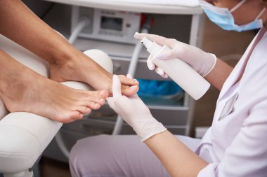 Genç kadın için pedikür yaparken sprey kullanarak profesyonel pedikürcü