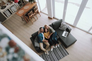 Mutlu ebeveynler dizüstü bilgisayar ile kanepede oturan ve kızlarını sarılma