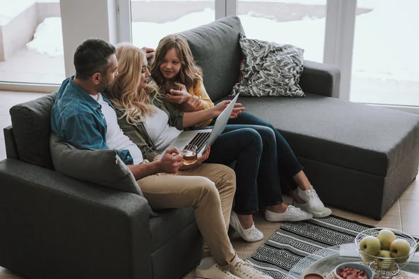 Šťastná rodina pije čaj a sledování videí v přenosném počítači doma — Stock fotografie
