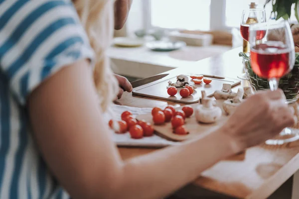 Man bereidt ingrediënten voor het diner terwijl Lady het houden van glas wijn — Stockfoto