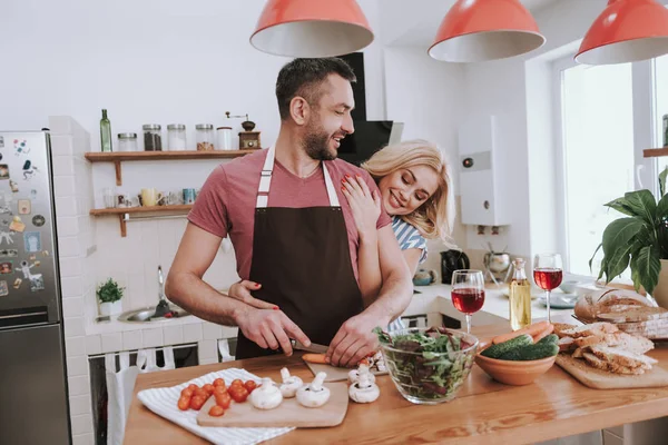 Affascinante signora bionda che abbraccia il marito da dietro mentre cucina la cena — Foto Stock