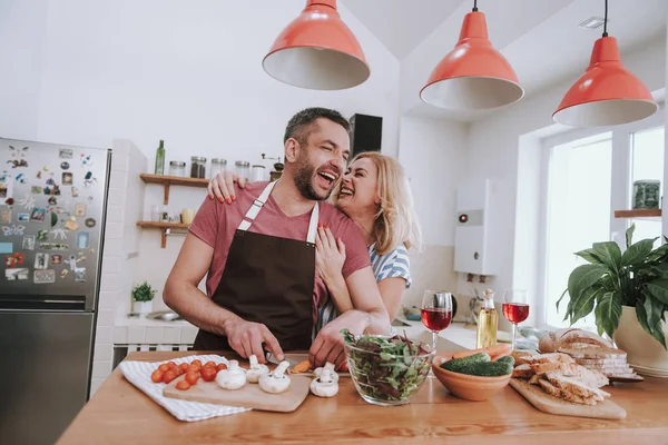 Glad blond dam kramar sin man bakifrån medan han matlagning middag — Stockfoto