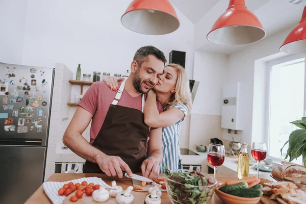 Charmante blonde dame zoenen man terwijl hij koken diner — Stockfoto