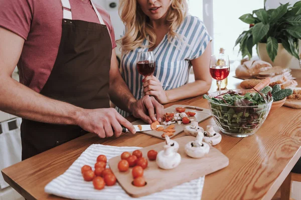 Blonde dame met drankje kijken hoe haar man koken diner — Stockfoto