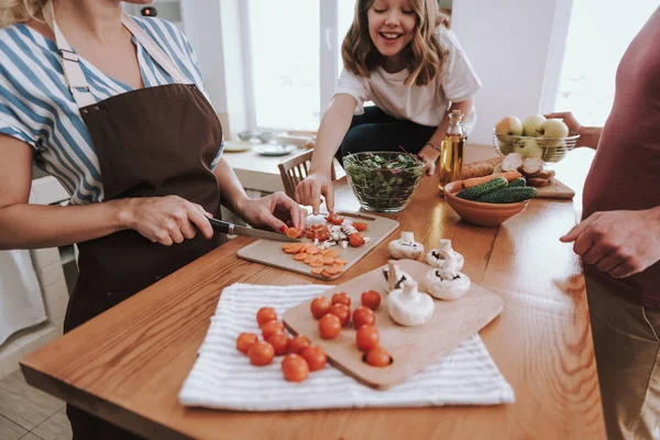 Schattig klein meisje neemt tomaat slice terwijl haar moeder koken diner — Stockfoto