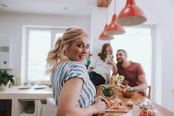 Vacker dam matlagning middag medan hennes man och dotter med hjälp av mobiltelefon — Stockfoto
