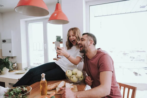 Vidám kislány és az apja néz vicces videókat a mobiloddal — Stock Fotó