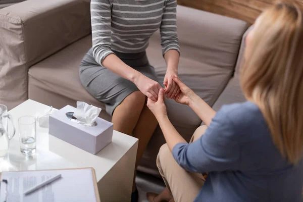 High angle of blonde female psychologist holding client arms during seance