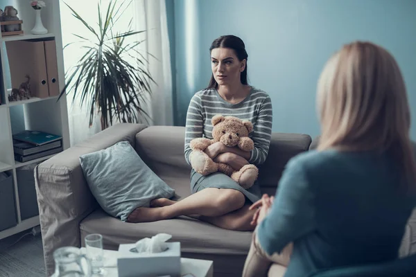 Unhappy brunette woman with teddy bear in arms looking away indoors — Stock Photo, Image