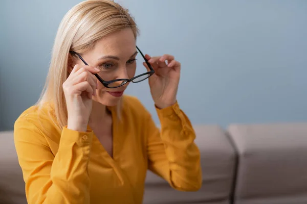 Lachende vrouwelijke psycholoog die een bril in armen houdt terwijl hij op de bank zit — Stockfoto