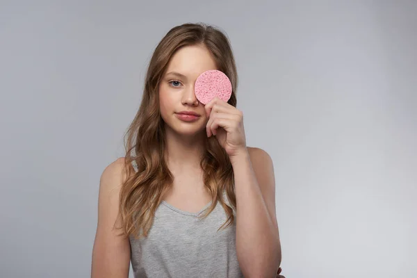 Urocza Nastoletnia dziewczyna pokrywająca oko z różową gąbką oczyszczającą — Zdjęcie stockowe