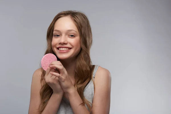 Menina adolescente alegre com esponja rosa em pé contra fundo cinza-branco — Fotografia de Stock