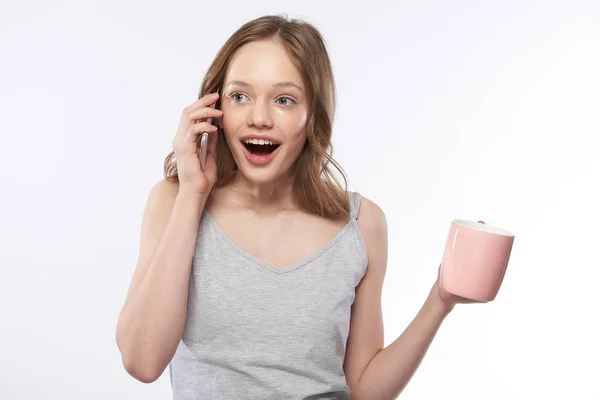 Nettes Teenie-Mädchen, das auf dem Handy spricht und eine rosa Tasse Kaffee in der Hand hält — Stockfoto