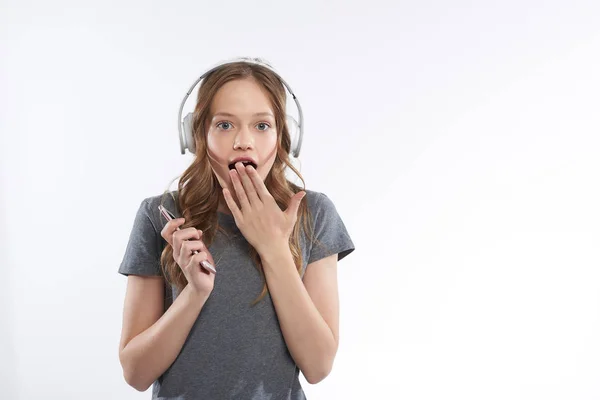 Šokovaná dívka v bezdrátových sluchátkách pokrývajících otevřenou pusu rukou — Stock fotografie