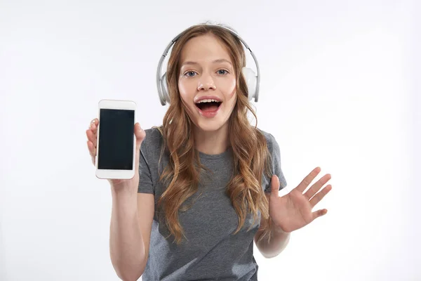 Hermosa chica adolescente en auriculares inalámbricos que demuestran el teléfono celular moderno — Foto de Stock