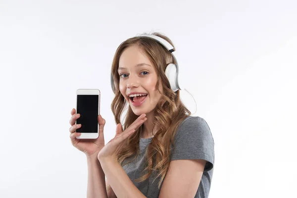 Roztomilá dívka v bezdrátových sluchátkách, která předvádí moderní mobil — Stock fotografie