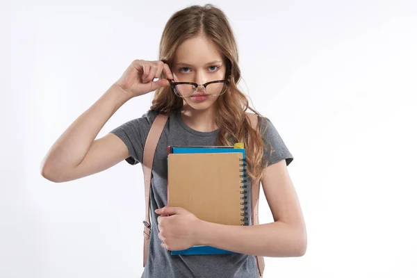 Schönes Teenie-Mädchen mit Spiralheft und Lehrbüchern, die die Brille abnehmen — Stockfoto