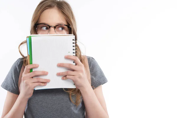 Menina adolescente bonito em óculos cobrindo rosto com caderno espiral — Fotografia de Stock