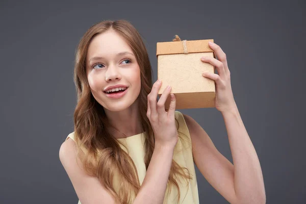 Красива дівчина-підліток трясе подарункову коробку і намагається вгадати, що приховано всередині — стокове фото