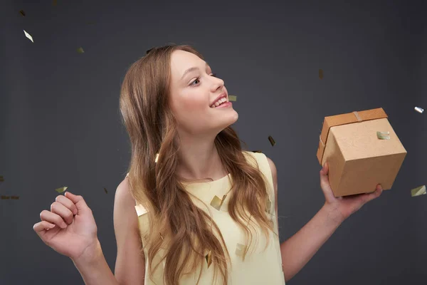 Hermosa chica adolescente en blusa amarilla sin mangas sosteniendo caja de regalo — Foto de Stock