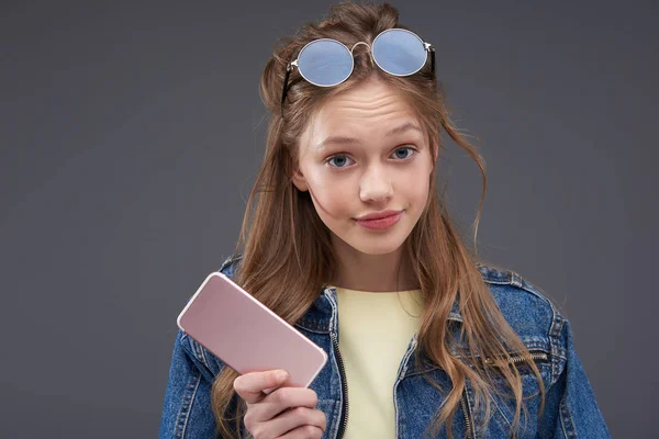 Geïrriteerd tiener meisje met bruin haar het houden van mobiele telefoon en streven lippen — Stockfoto