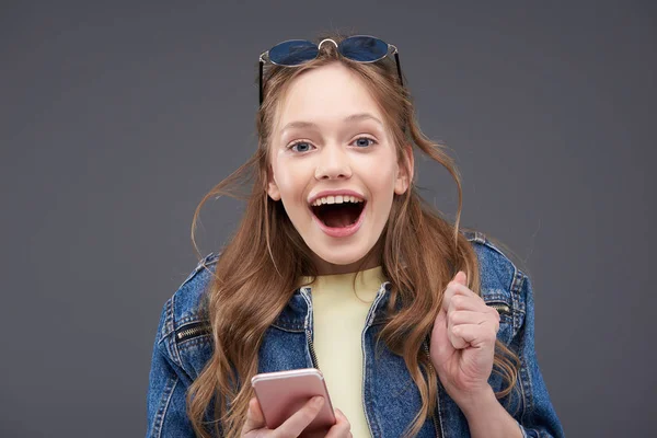 Vrolijke tiener meisje in Jean jas Holding roze mobiele telefoon — Stockfoto