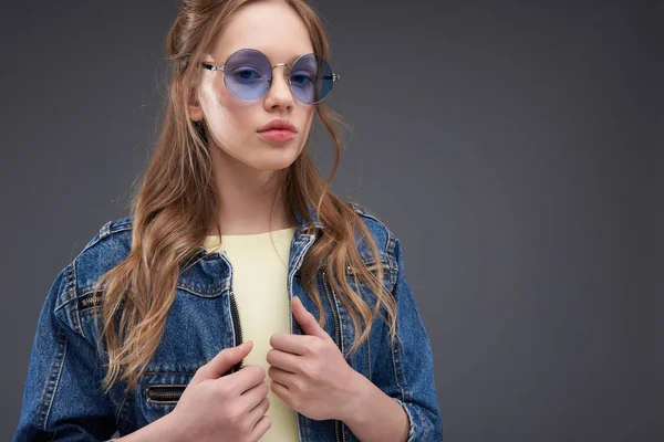 Schönes Teenie-Mädchen in Jeansjacke steht vor blaugrauem Hintergrund — Stockfoto