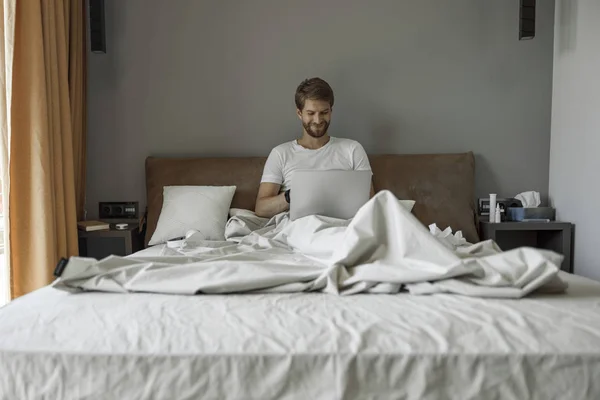 Sonriente hombre trabajando remotamente desde su cama — Foto de Stock