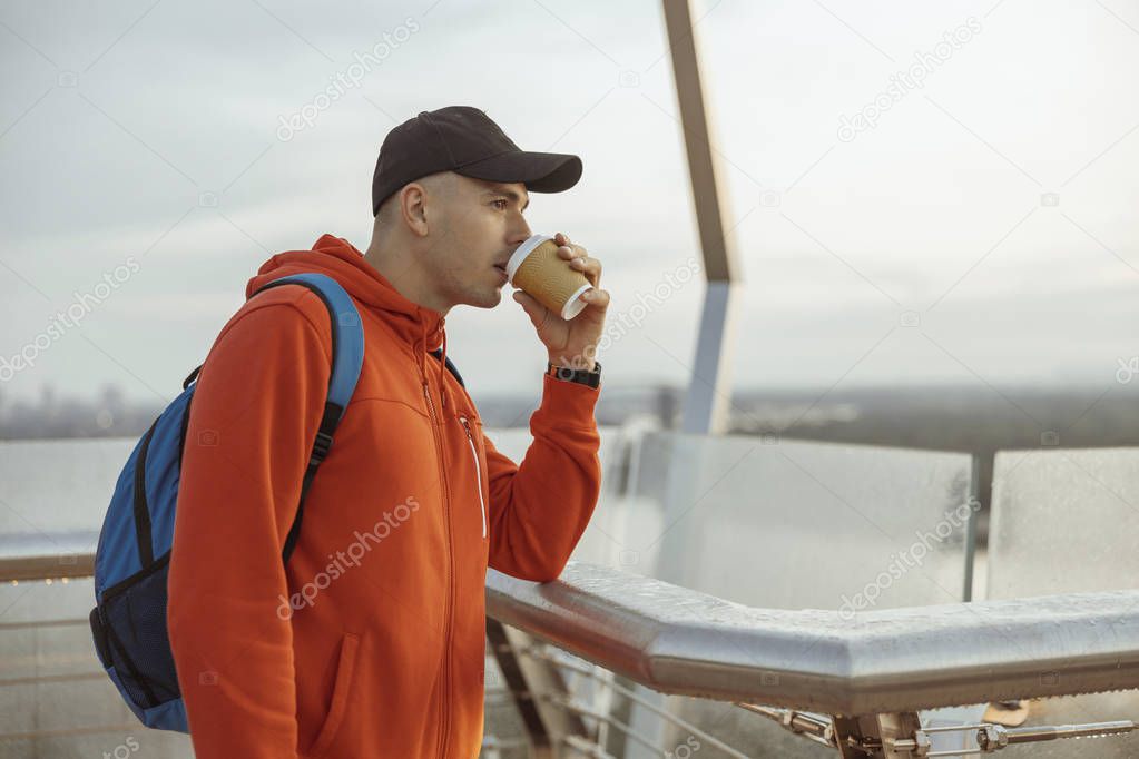 Serious sportsman drinking coffee on a bridge