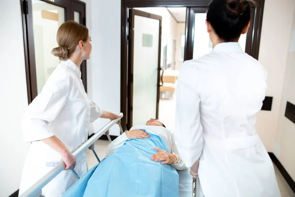 Dos enfermeras transportando al paciente en la clínica foto de stock — Foto de Stock