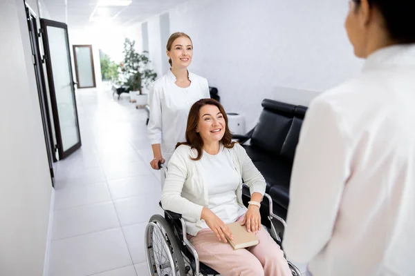 診療所の女性ストック写真で障害者を運ぶ笑顔の看護師 — ストック写真