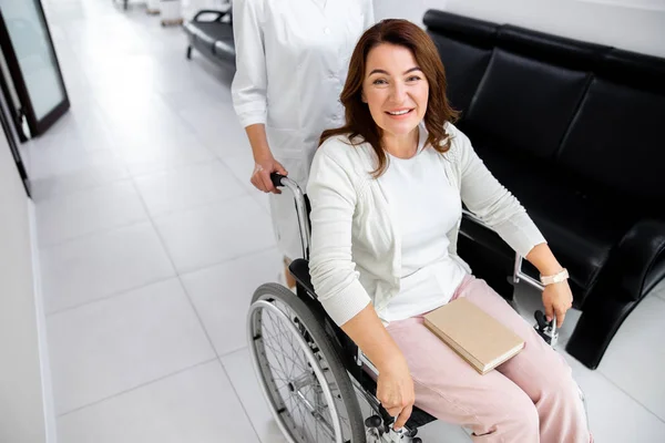 Joyeuse dame en fauteuil roulant poussé par infirmière photo de stock — Photo