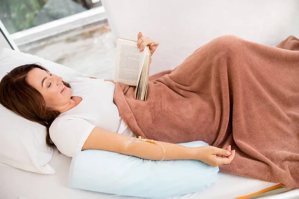 Glimlachend volwassen vrouwelijke lezing boek in bed — Stockfoto